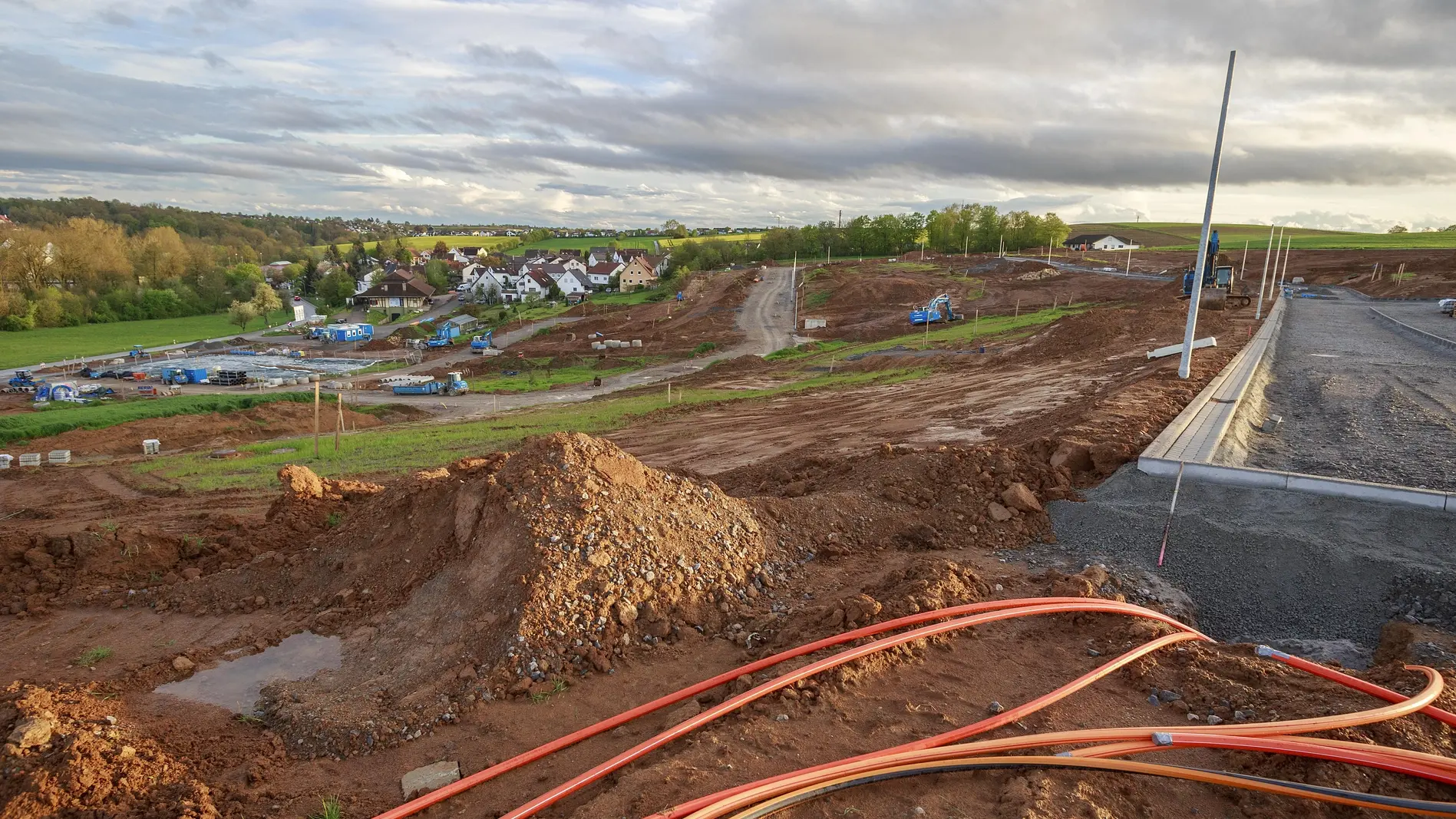 Baustelle in einem Neubaugebiet, im Vordergrund liegen Glasfaserkabel auf dem Boden