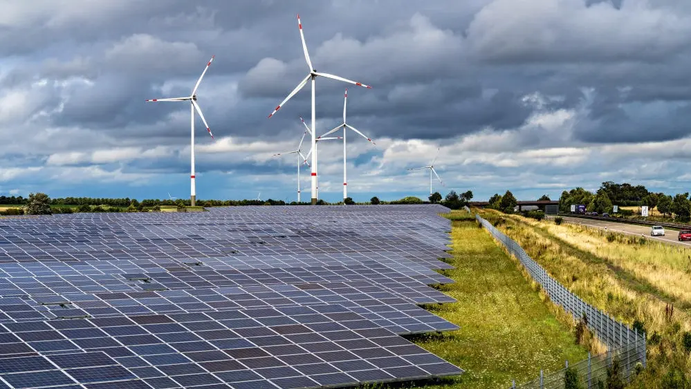 Eine Photovoltaikanlage auf einem Feld, im Hintergrund stehen Windräder
