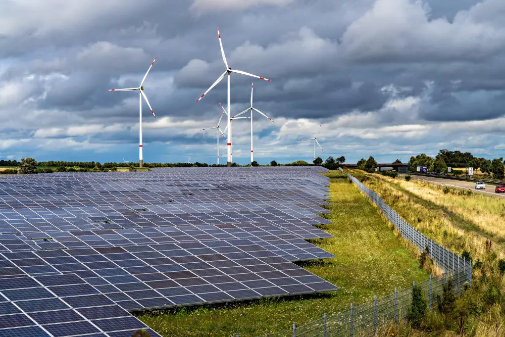 Eine Photovoltaikanlage auf einem Feld, im Hintergrund stehen Windräder