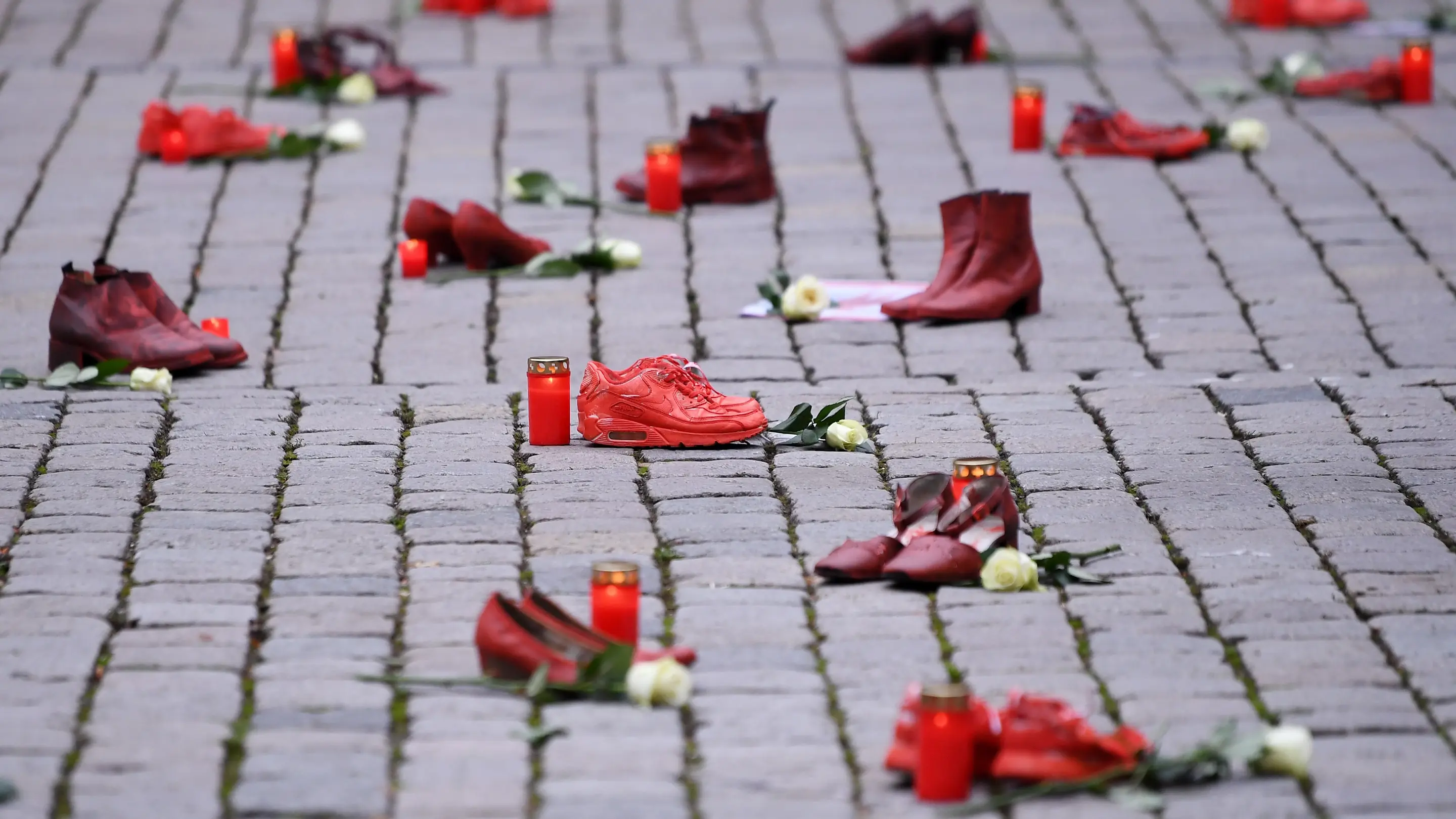 Gewalt an Frauen Rote Schuhe mit Grablichtern und weißen Rosen auf einem Gehweg