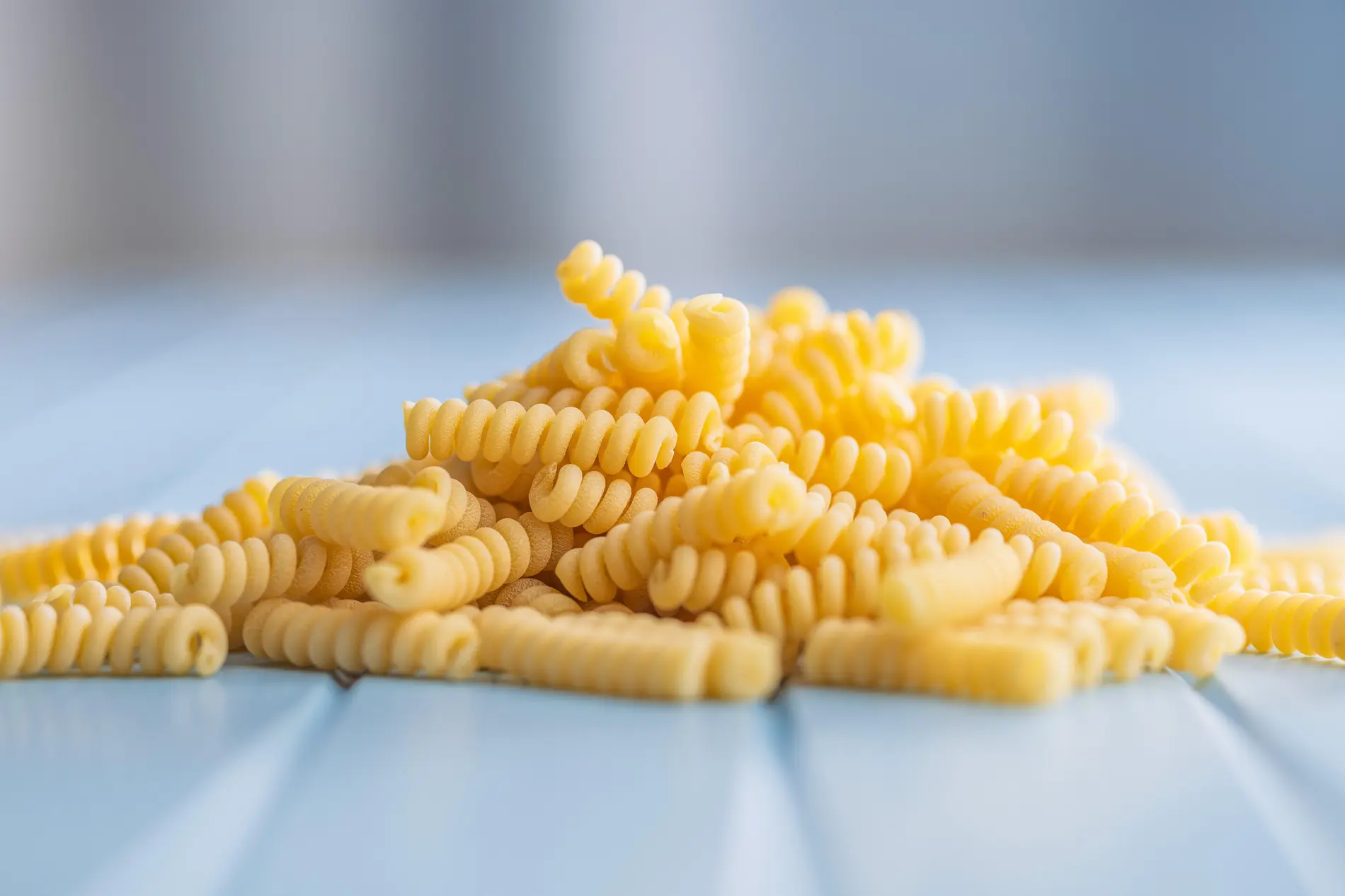 Ungekochte Fusilli-Nudeln auf einem blauen Tisch.