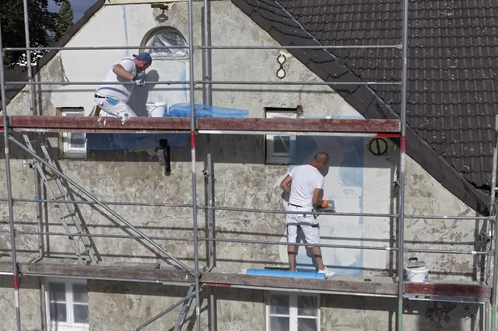 Maler auf Gerüst verputzen die Fassade an einem Haus von 1830
