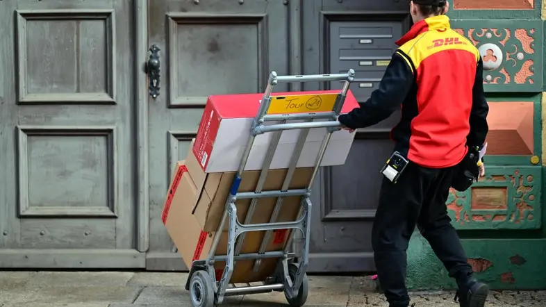 Ein DHL Mitarbeiter liefert Paketsendungen mit einer Sackkarre aus