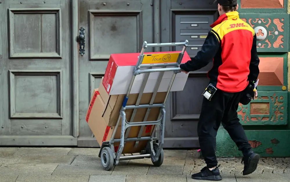 Ein DHL Mitarbeiter liefert Paketsendungen mit einer Sackkarre aus