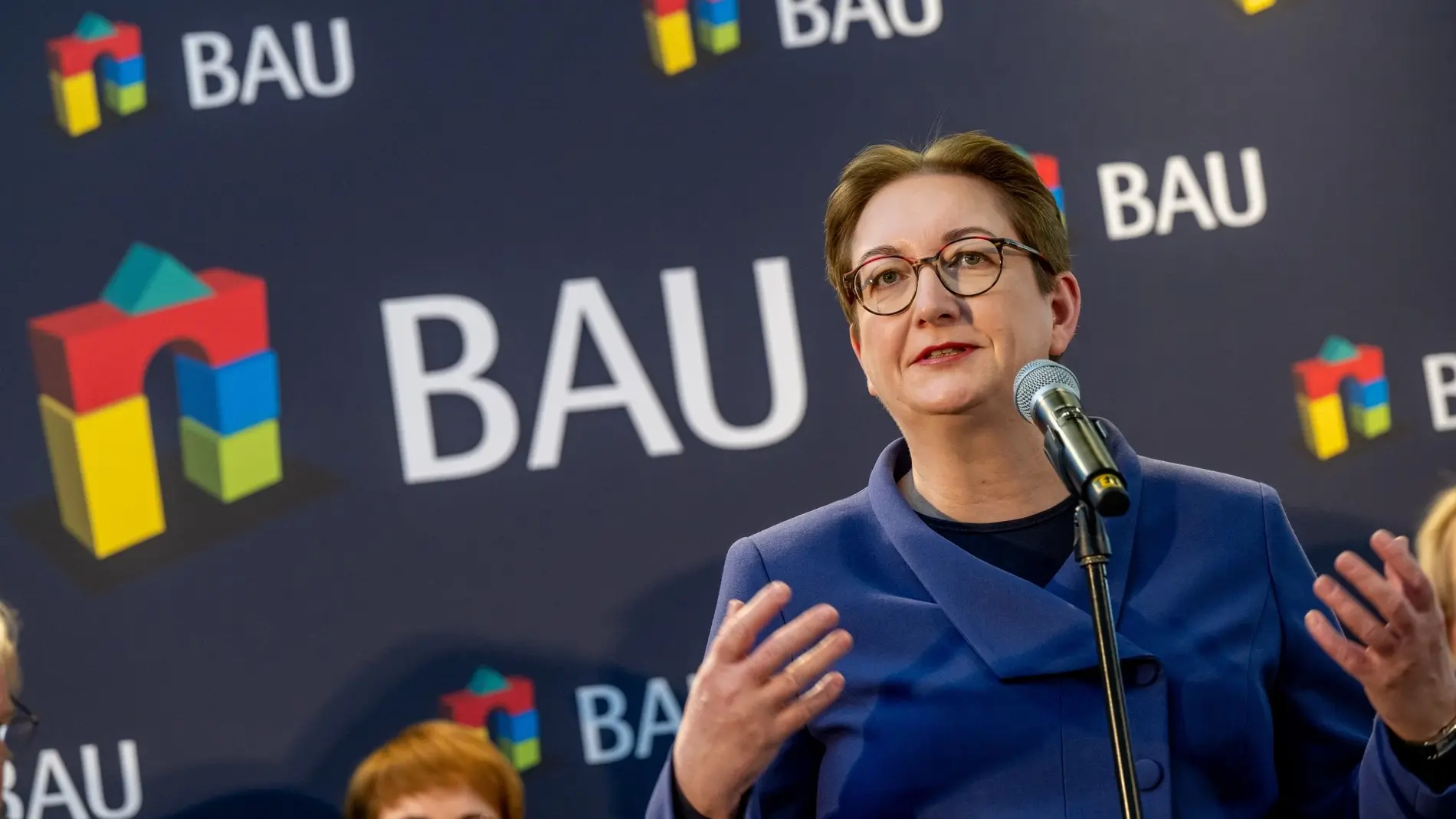 Klara Geywitz im blauen Blazer und mit Brille am Rednerpult der Baumesse