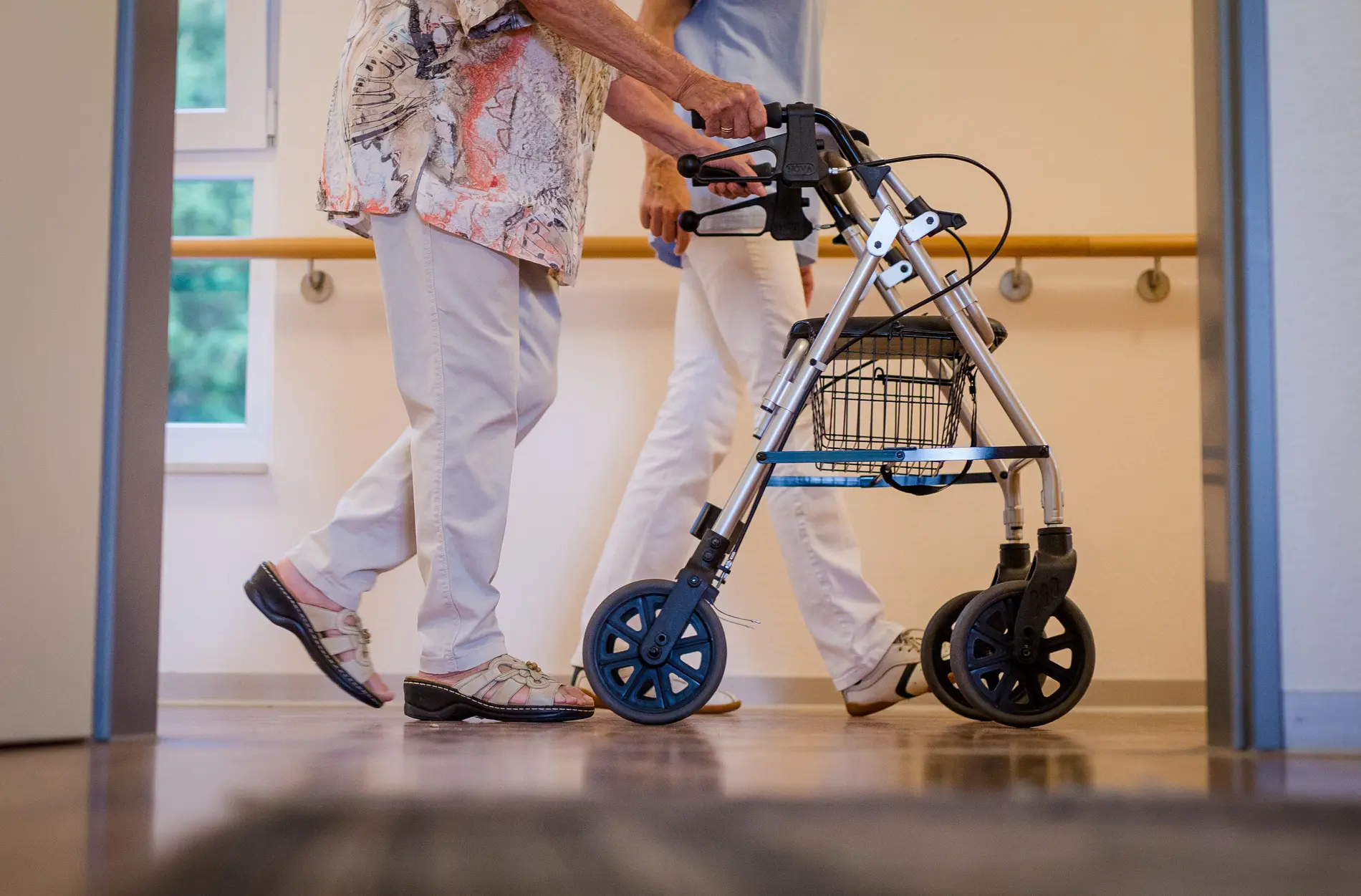 Anhörung zur Pflegekompetenz Eine Pflegekraft geht in einem Pflegeheim mit einer älteren Dame über einen Korridor.