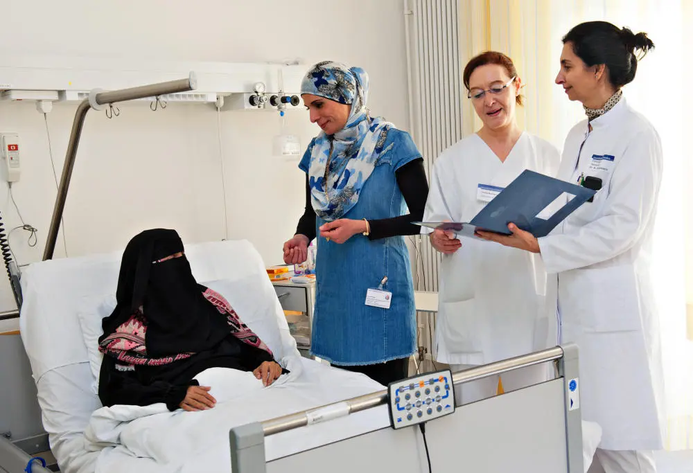 Drei Krankhausmitarbeiterinnen stehen am Bett von Patientin in einem Niqab.