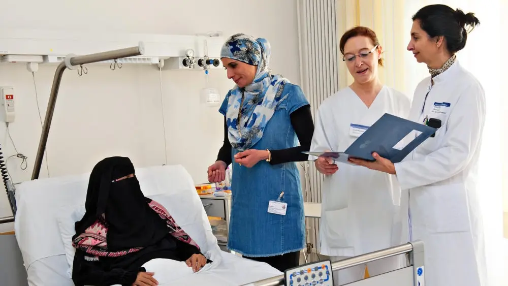 Drei Krankhausmitarbeiterinnen stehen am Bett von Patientin in einem Niqab.