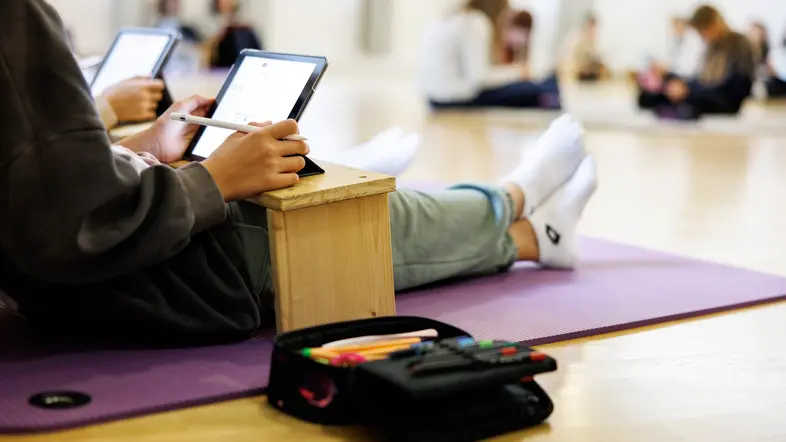 Schülerin sitzt mit Tablet auf dem Boden