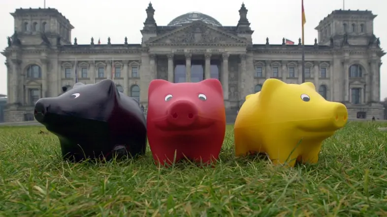 Drei Schweinchenfiguren (schwarz, rot und gold) stehen im Gras vor dem Reichstagsgebäude