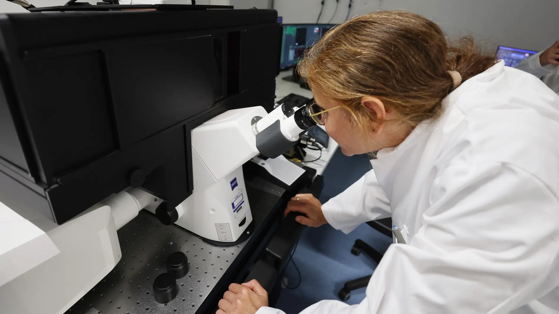 Wissenschaftliche Mitarbeiterin schaut in ein Mikroskop in einem Forschungsraum.