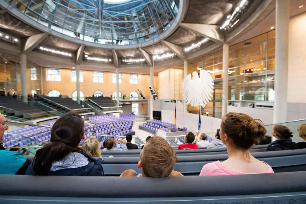 Menschen sitzen auf der Besuchertribüne im Plenarsaal des Deutschen Bundestags. 