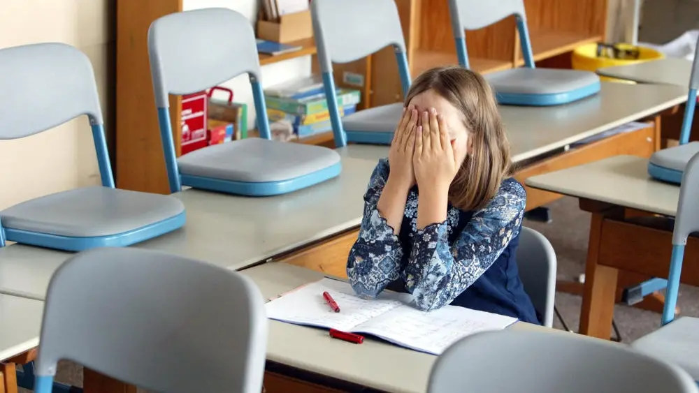 Eine Schülerin sitzt im Klassenzimmer und verdeckt das Gesicht mit ihren Händen.