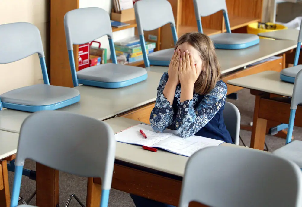 Eine Schülerin sitzt im Klassenzimmer und verdeckt das Gesicht mit ihren Händen.