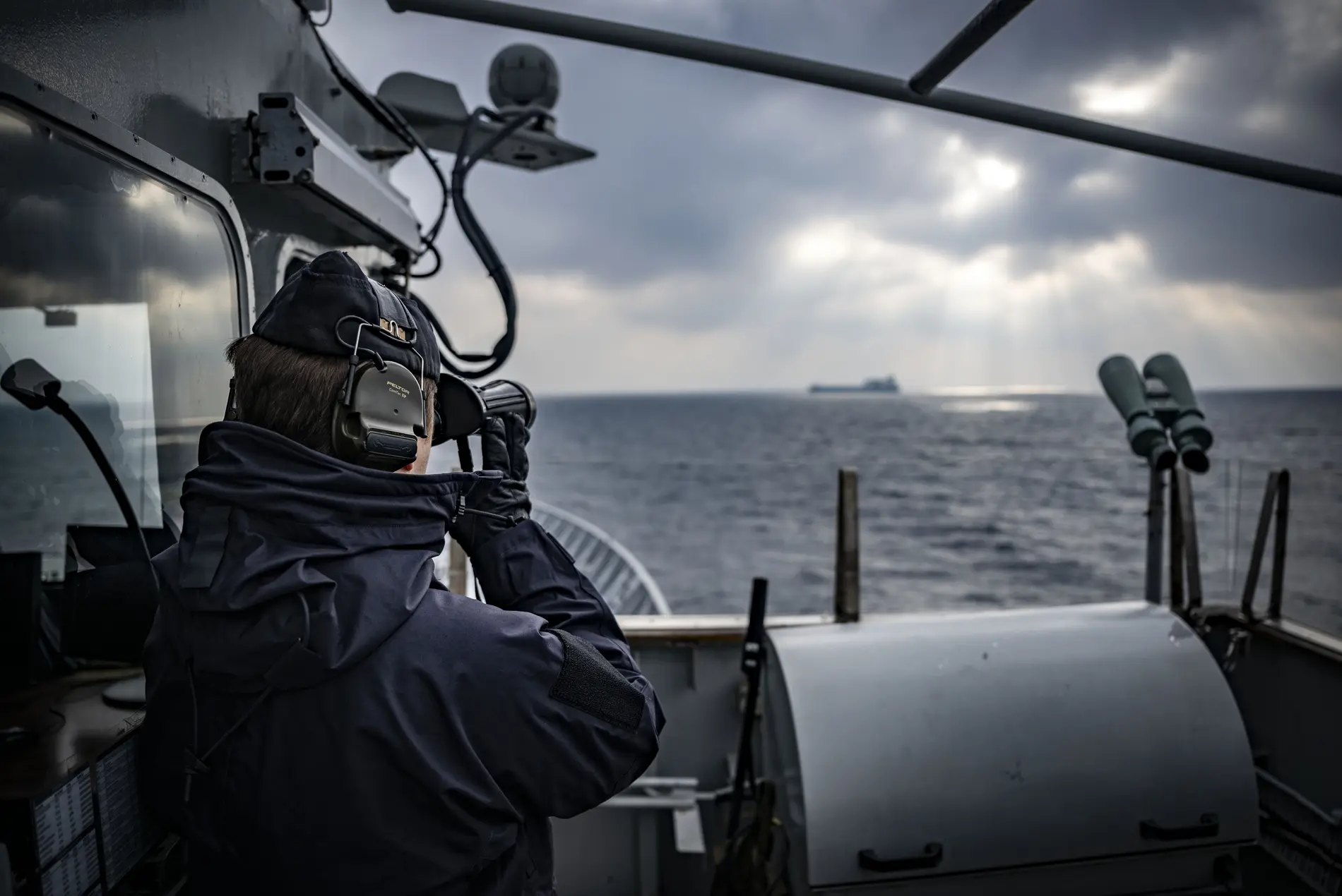 Operation Baltic Sentry Person beobachtet ein Frachtschiff durch ein Fernglas