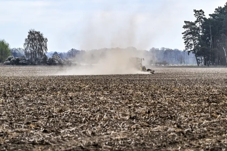 Auf einem Feld fährt ein Traktor über ein trockenes Feld und wirbelt dabei viel staubige, trockene Erde auf.