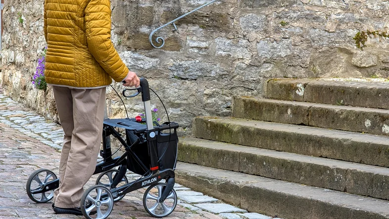 Eine Person mit Rollator steht vor Treppen
