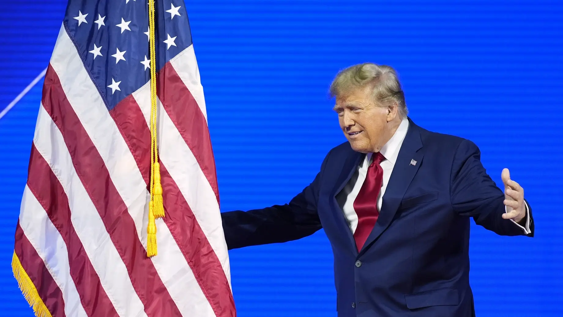 Donald Trump umarmt die amerikanische Fahne Donald Trump mit ausschweifender Handgeste neben der USA-Flagge