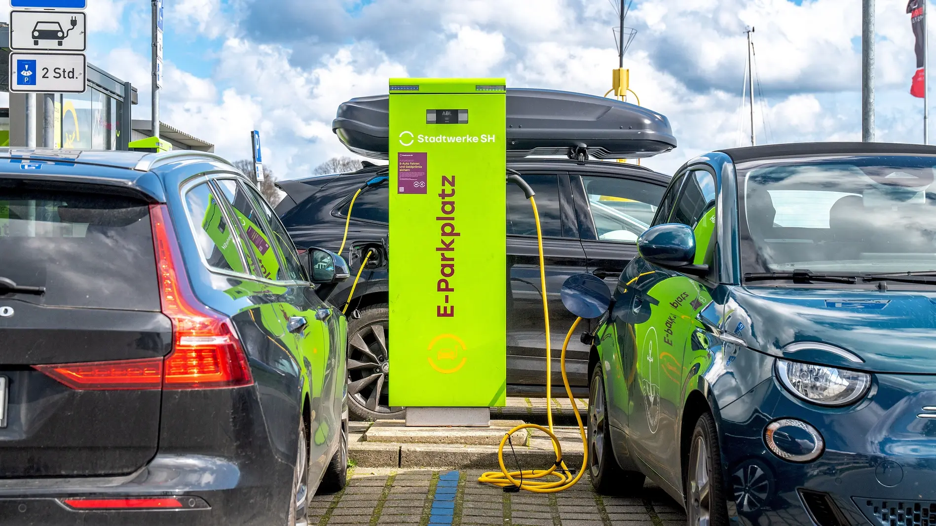 Grüne Ladesäule für Elektroautos Ein elektrischer Volvo und ein elektrischer Fiat 500 stehen zum Aufladen an einer grünen Ladesäule.