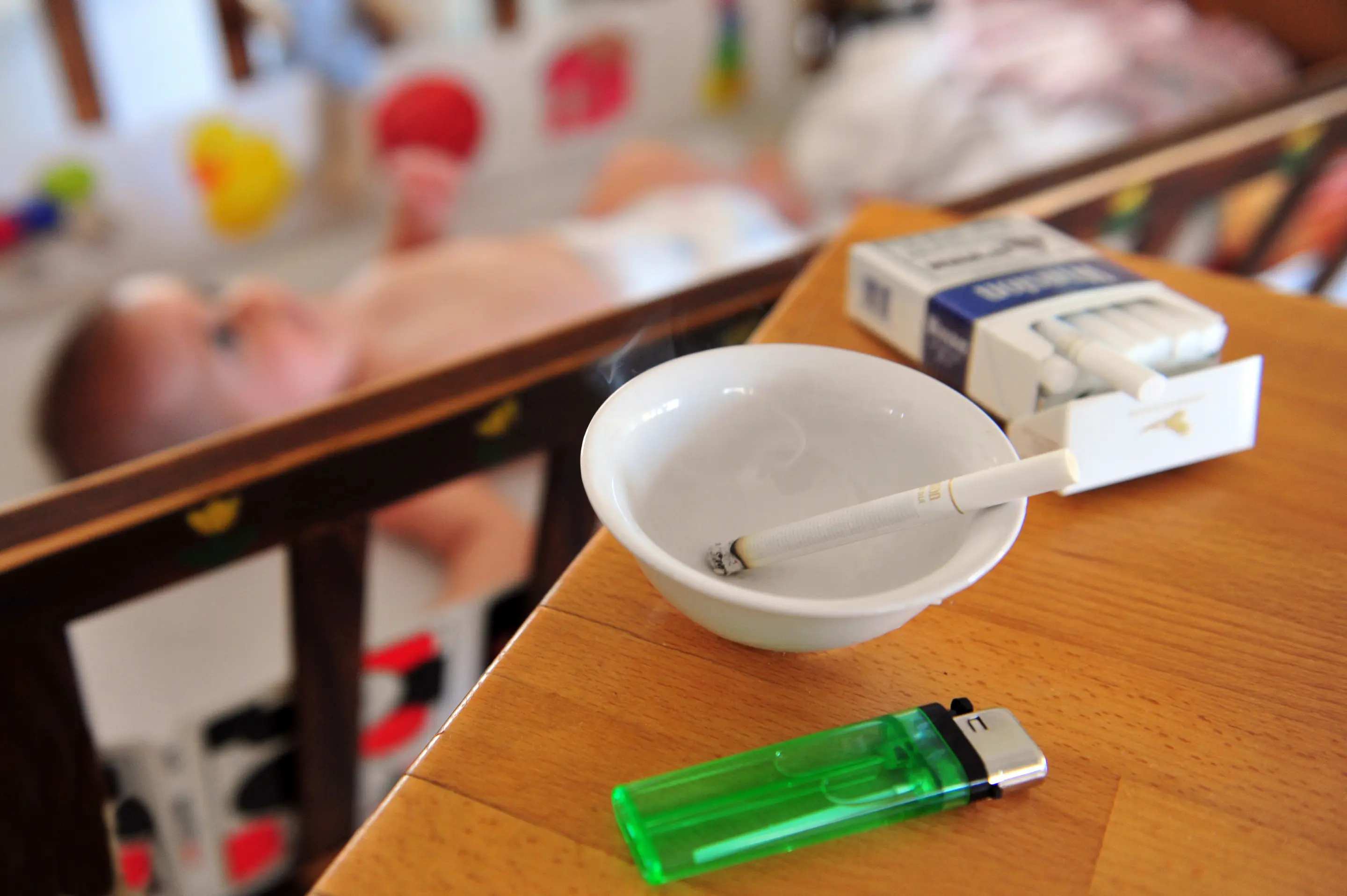 Kinder werden zu Mitrauchern Zigarettenschachtel, Aschenbecher und Feuerzeug vor einer Krippe mit Baby.