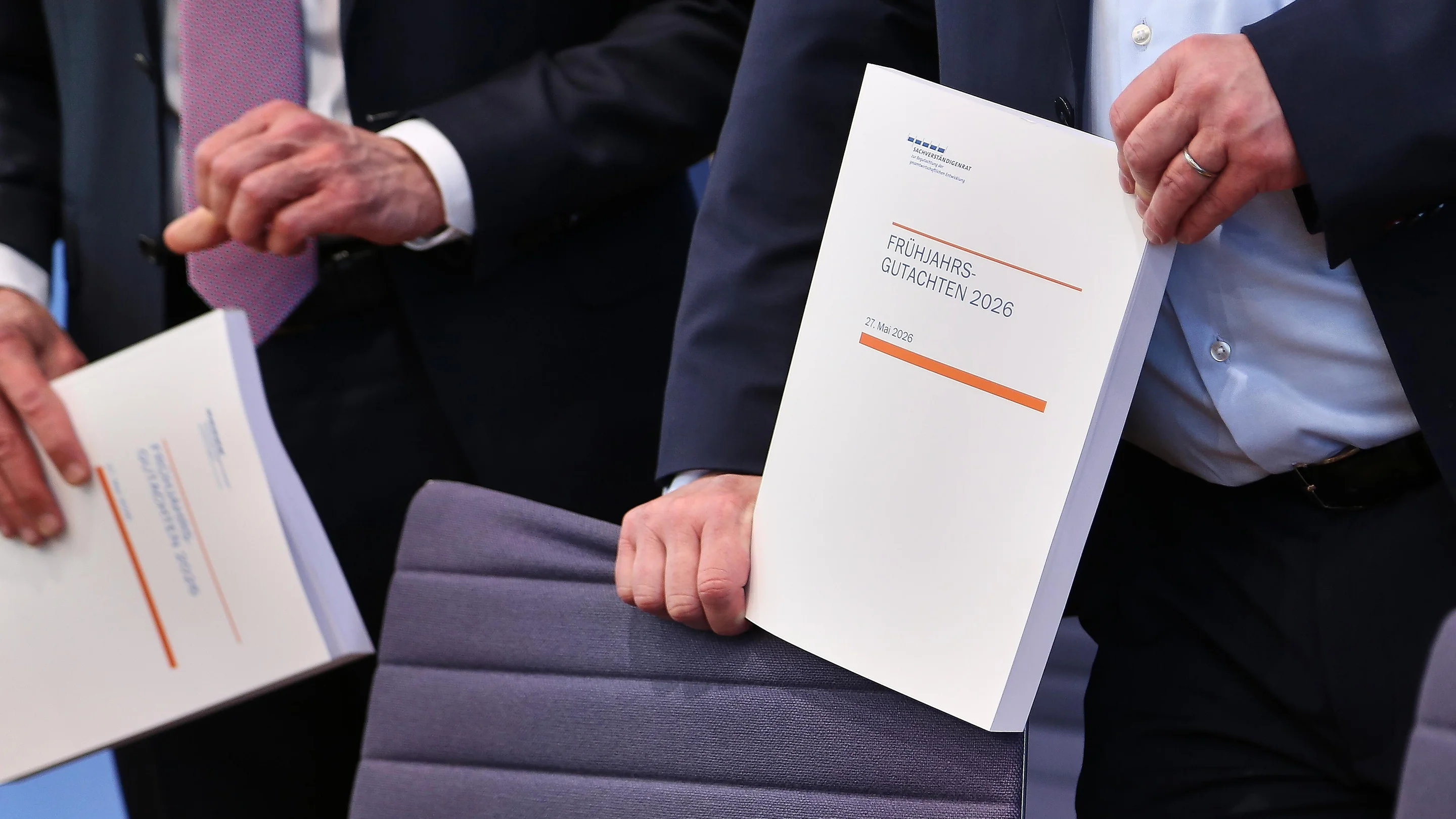 Zwei Paar Hände halten das Frühjahrsgutachten 2026 der Wirtschaftsweisen