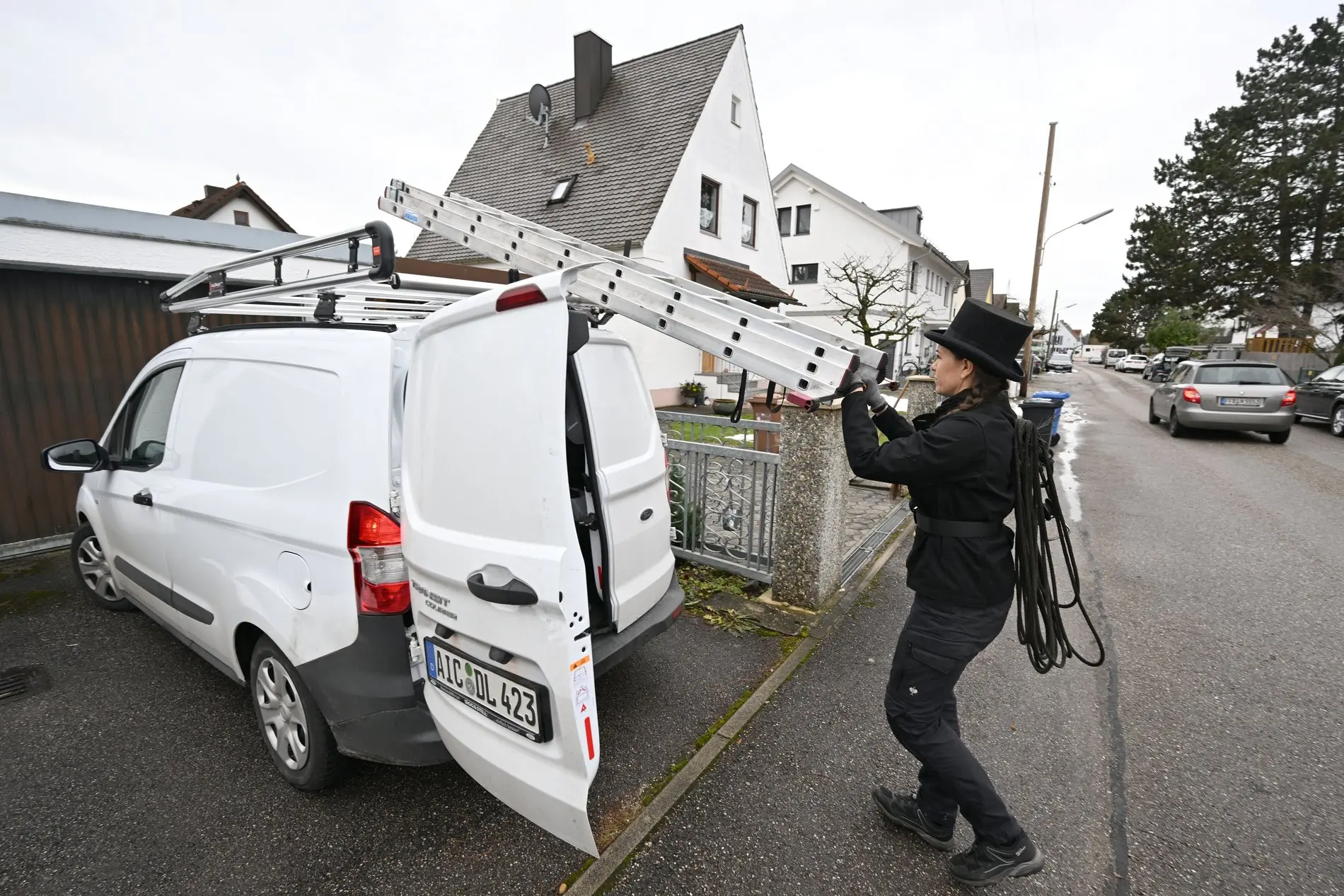 Das Bild zeigt einen Schornsteinfeger, der sein Auto belädt.