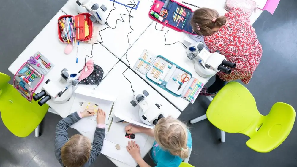 Schülerinnen der Universitätsschule arbeiten an Mikroskopen.