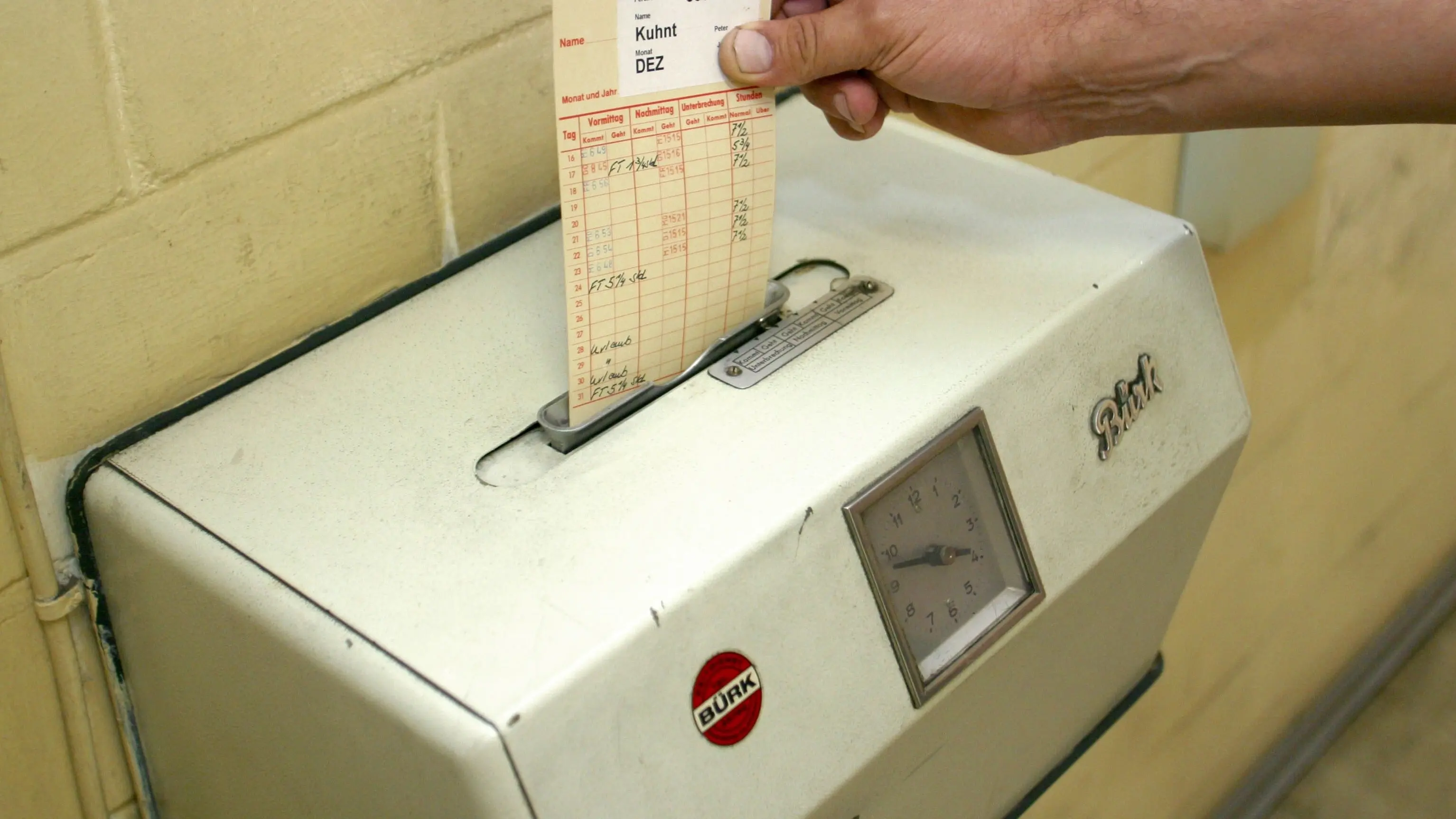 Hand steckt Stempelkarte in Stechuhr