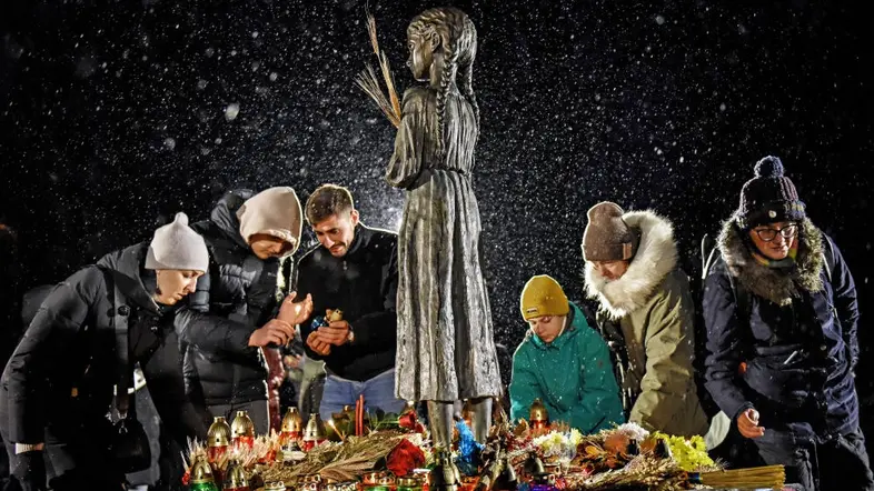 Sechs Menschen stehen um ein Mahnmal versammelt.