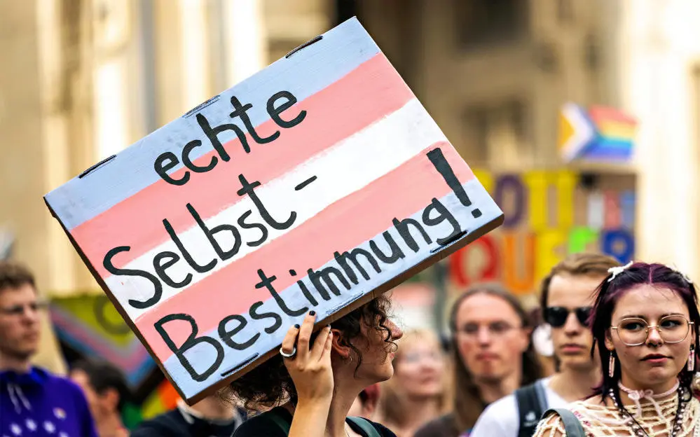 Foto einer Demonstration für das Selbstbestimmungsgesetz Bild eines Demoschildes in den Farben der trans Pride-Flagge mit der Inschrift "echte Selbstbestimmung"