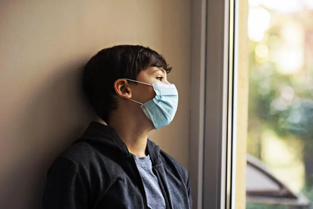 Corona-Pandemie Kleiner Junge mit medizinischer Maske lehnt an einer Wand
