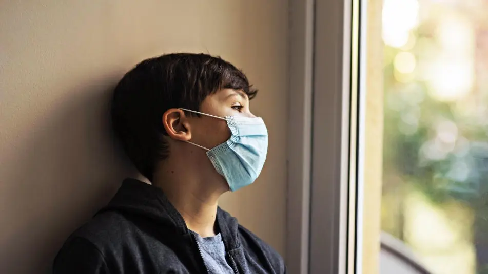 Kleiner Junge mit medizinischer Maske lehnt an einer Wand