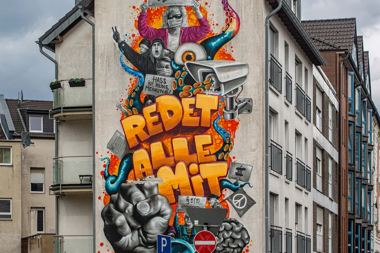 Großformatiges Mural mit dem Titel "Redet alle mit" auf einer Hauswand