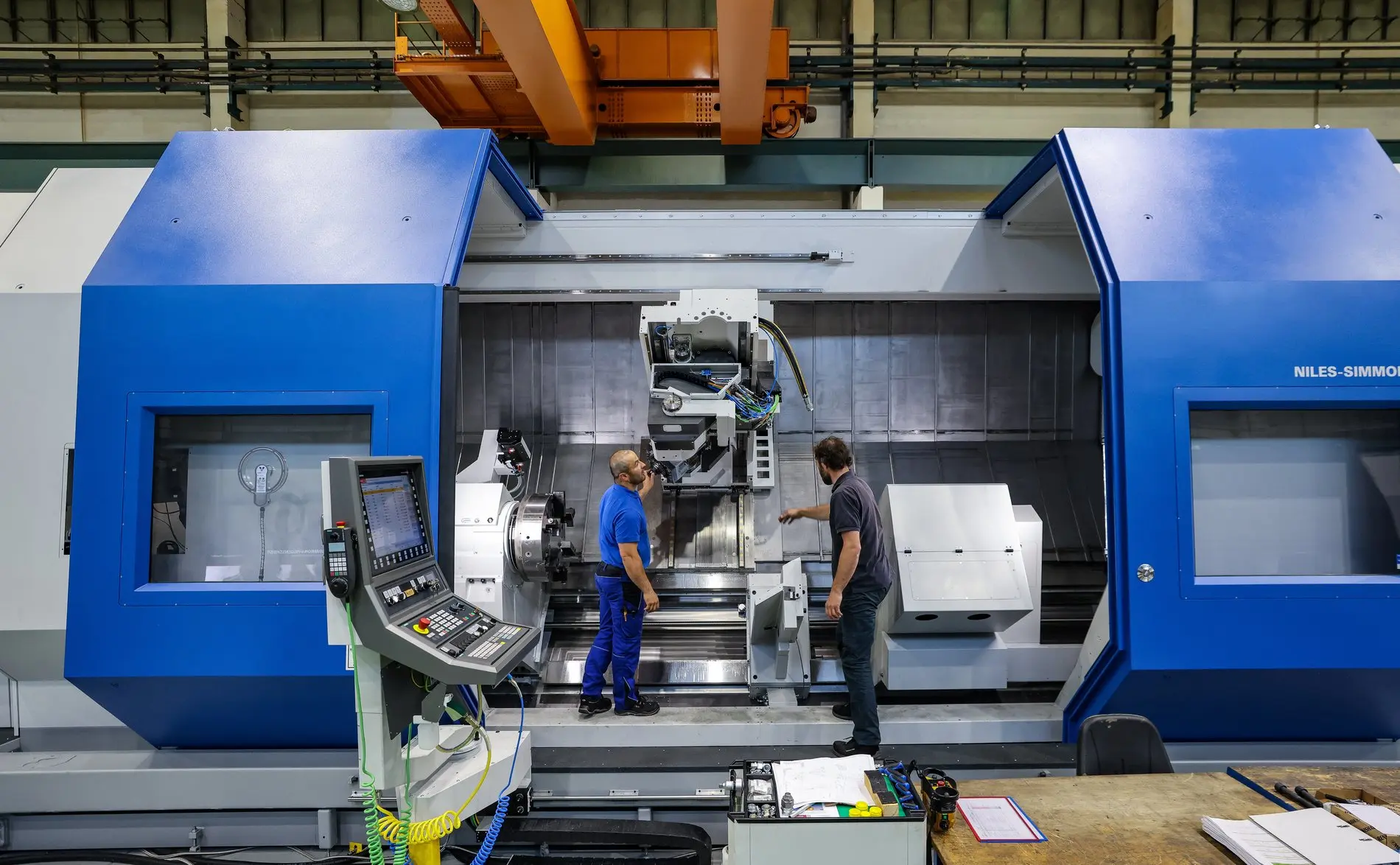 Zwei Mitarbeiter stehen an einer Industrieanlage, bedienen eine Maschine.