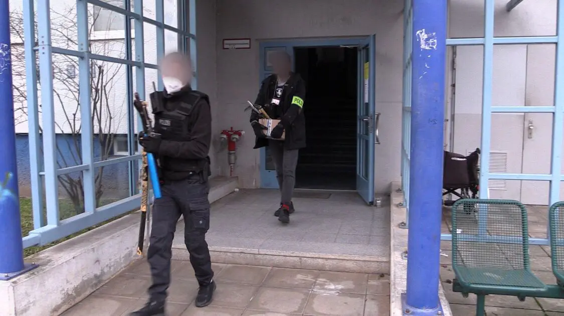 Polizisten verlassen mit beschlagnahmten Gegenständen ein Haus