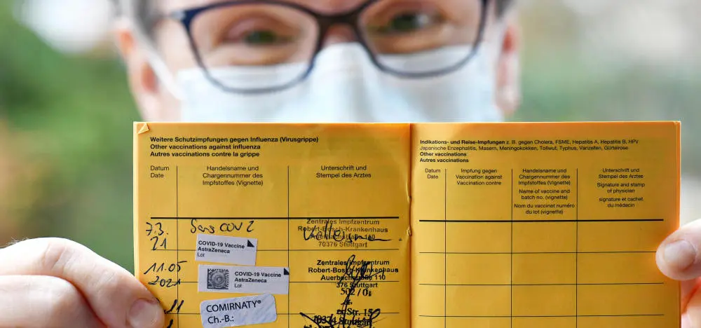 Gestempelter Impfpass wird von Person mit Brille, medizinischer Maske gehalten