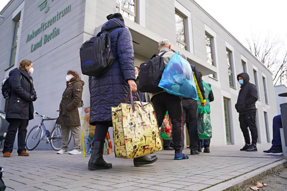 Menschen mit Taschen und Rucksäcken stehen vorm Ankunftszentrum für Geflüchtete