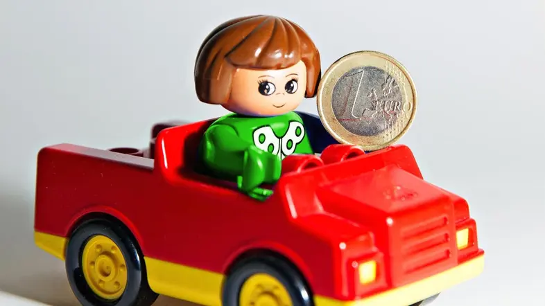 Spielzeugfigur sitzt im Spielzeugcabrio und hält eine 1 Euromünze