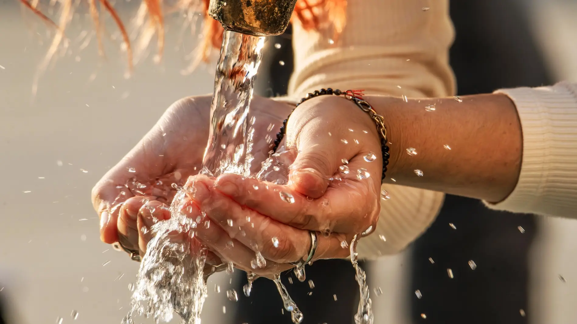 Ohne Wasser geht nichts im Körper Frau schöpft mit ihren Händen Trinkwasser aus einem Brunnen