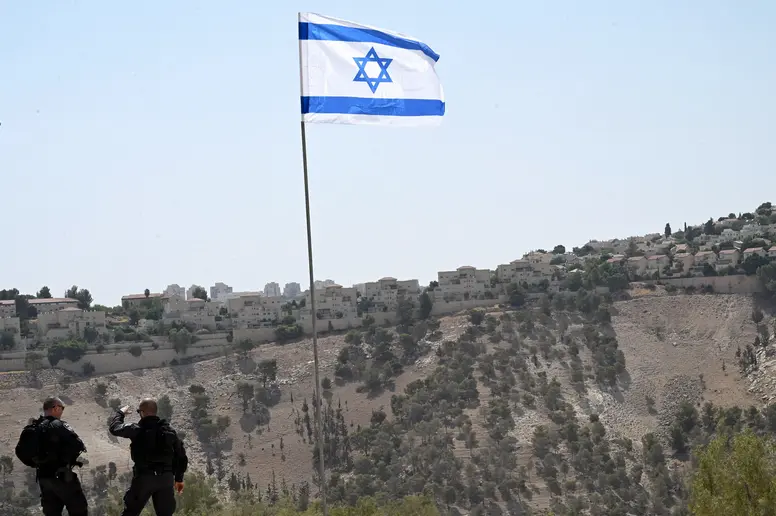 Israelische Soldaten stehen vor einer Israel-Flagge in einem brachen Terrain
