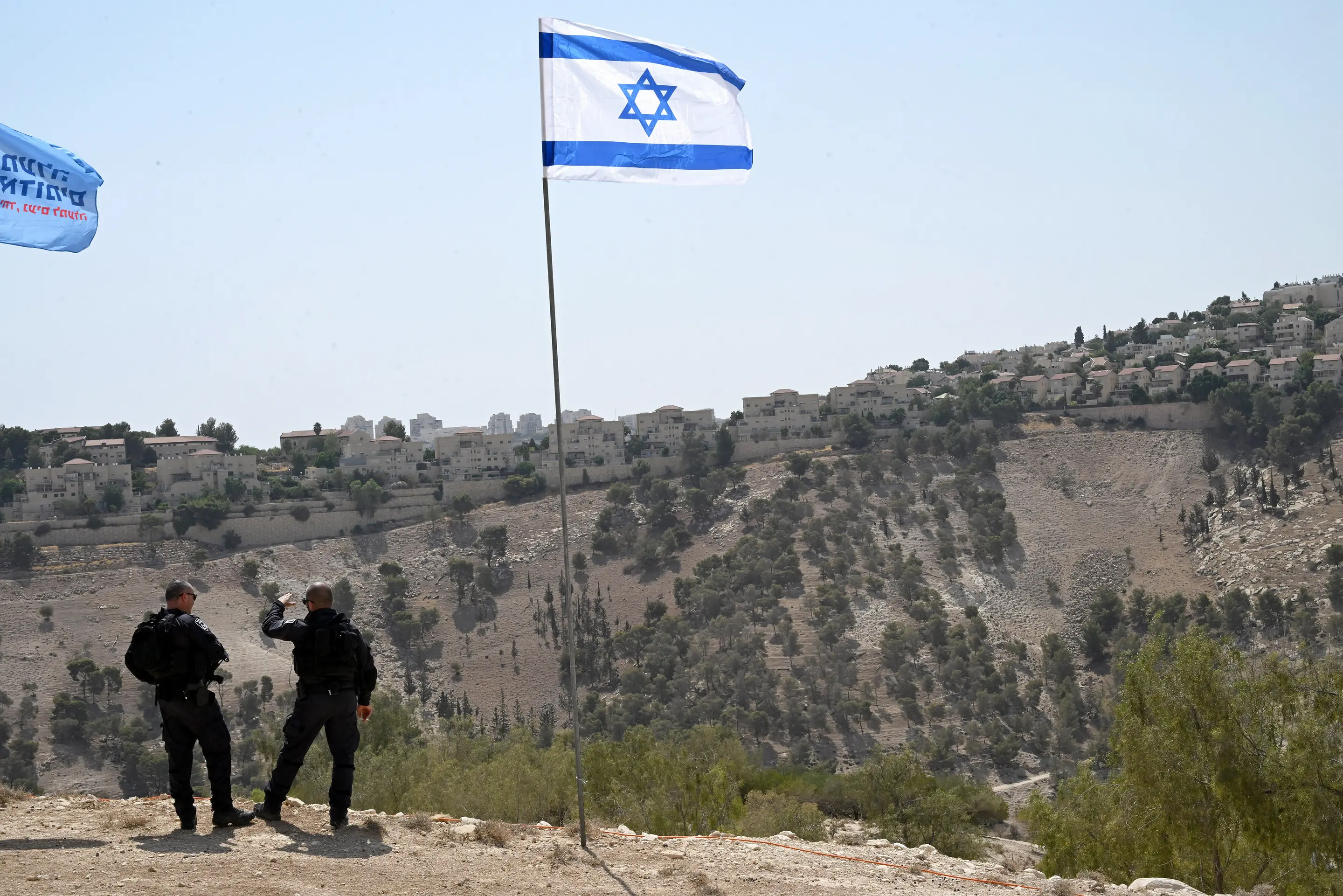 Israelische Soldaten stehen vor einer Israel-Flagge in einem brachen Terrain