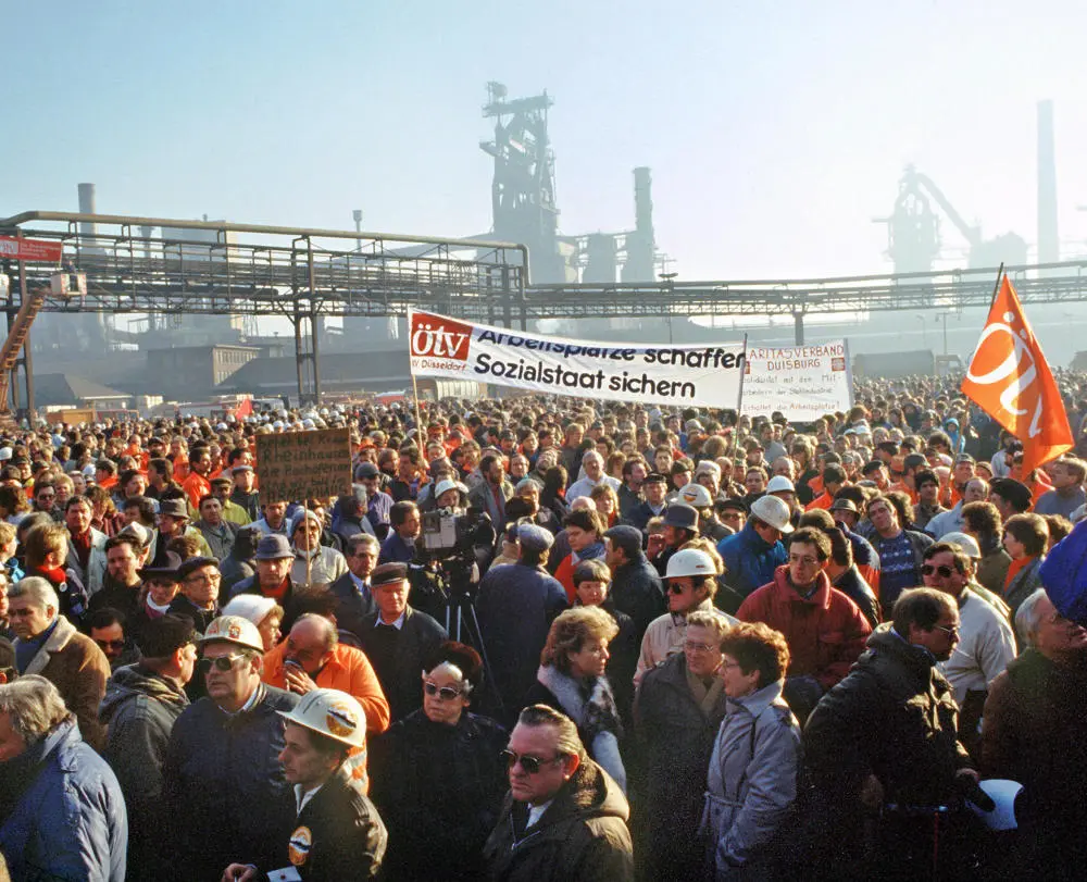 Demonstranten versammeln sich, Stahlwerk im Hintergrund.