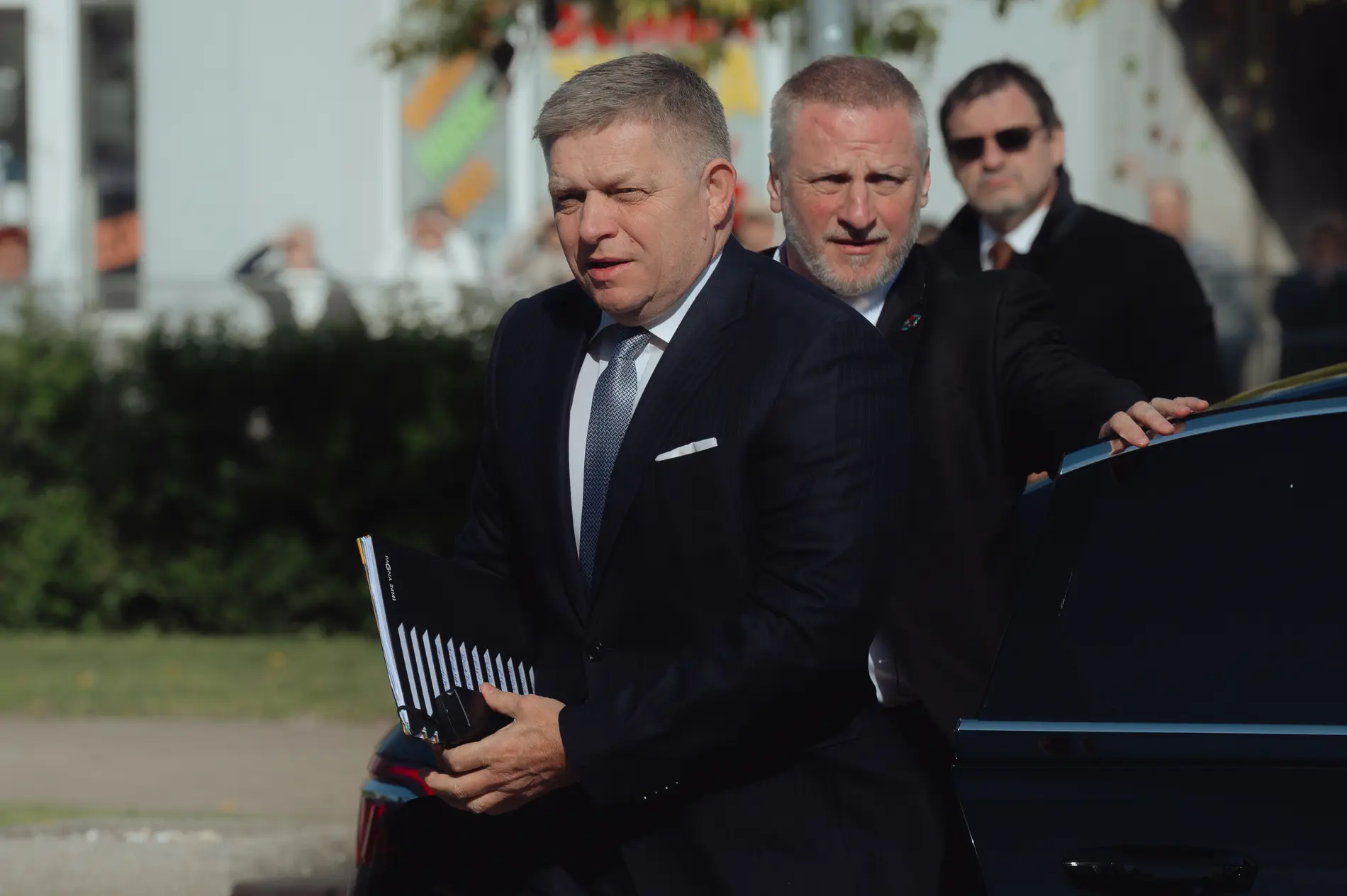 Robert Fico mit einer Akte vor einem Auto