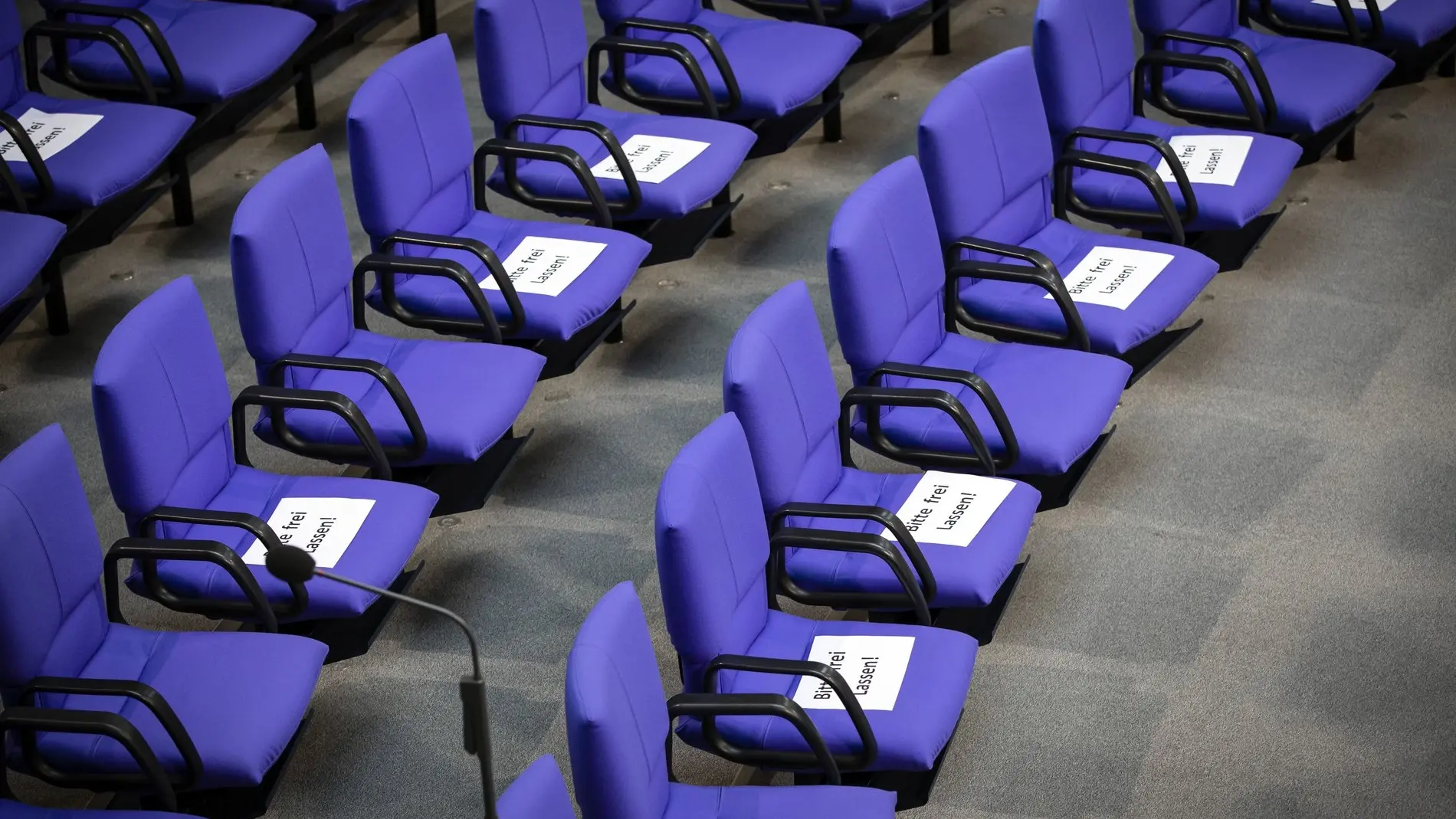 Leere Stühle mit Hinweisen "Bitte freilassen" im Plenarsaal.