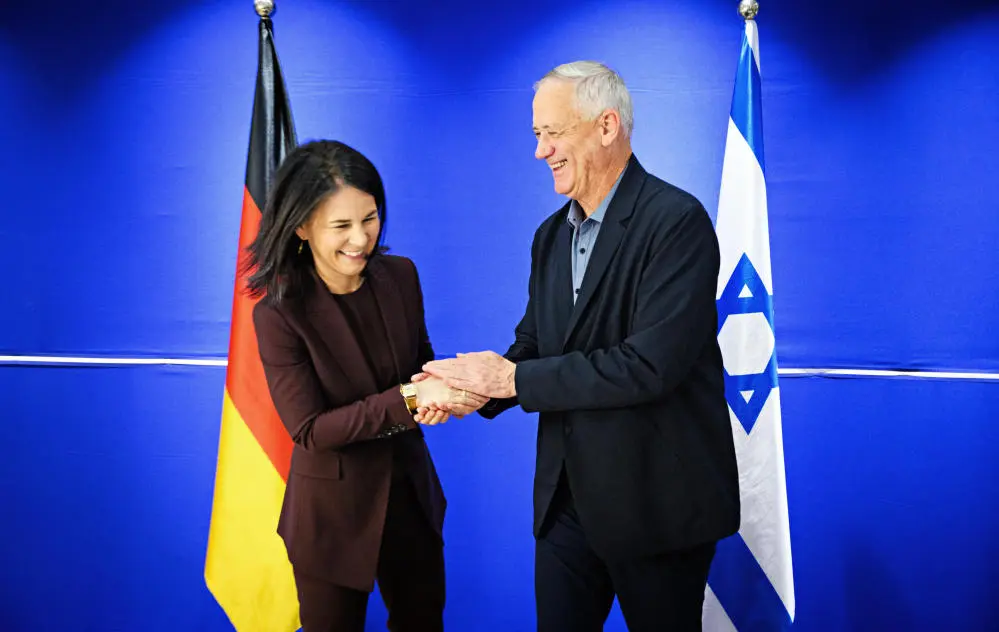 Annalena Baerbock und Benny Gantz geben sich die Hand vor den Länderflaggen