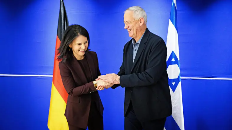 Annalena Baerbock und Benny Gantz geben sich die Hand vor den Länderflaggen