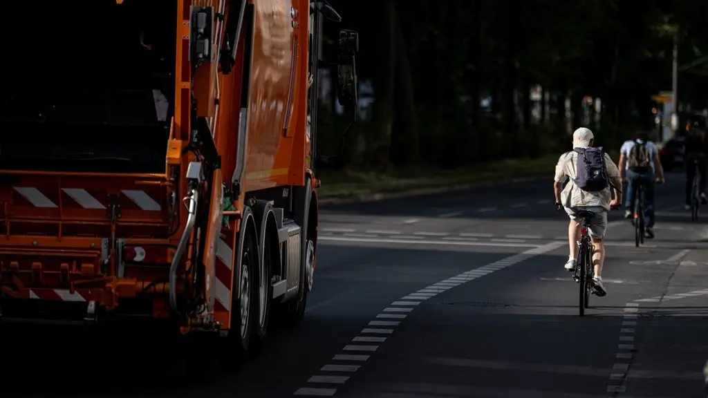 Ein Wagen der Müllabfuhr fährt neben einem Radfahrer auf der Straße.