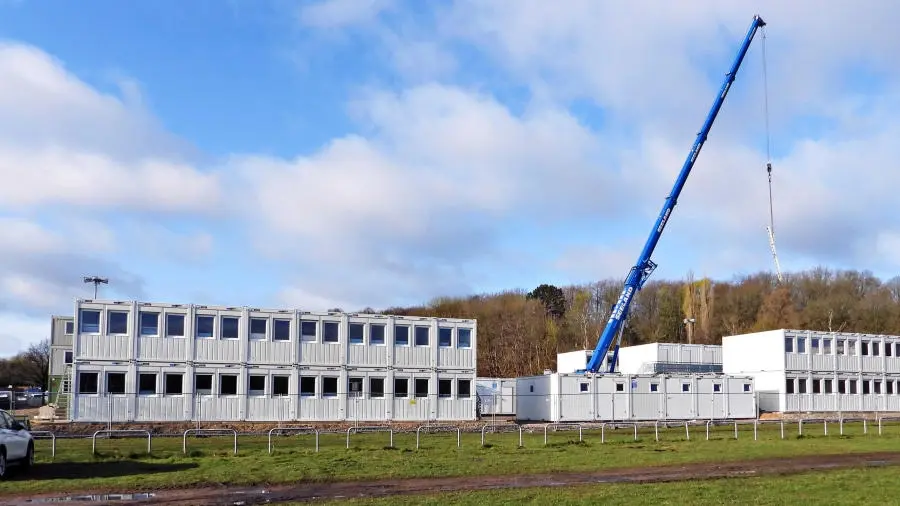 Unterkunft aus Containern Ein blauer Kran stapelt weiße Wohncontainer übereinander.
