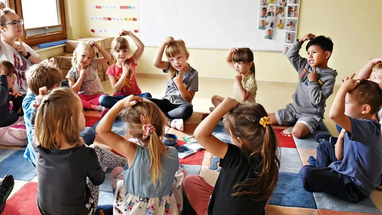 Kinder und Erzieherin sitzen im Kreis auf dem Fußboden.