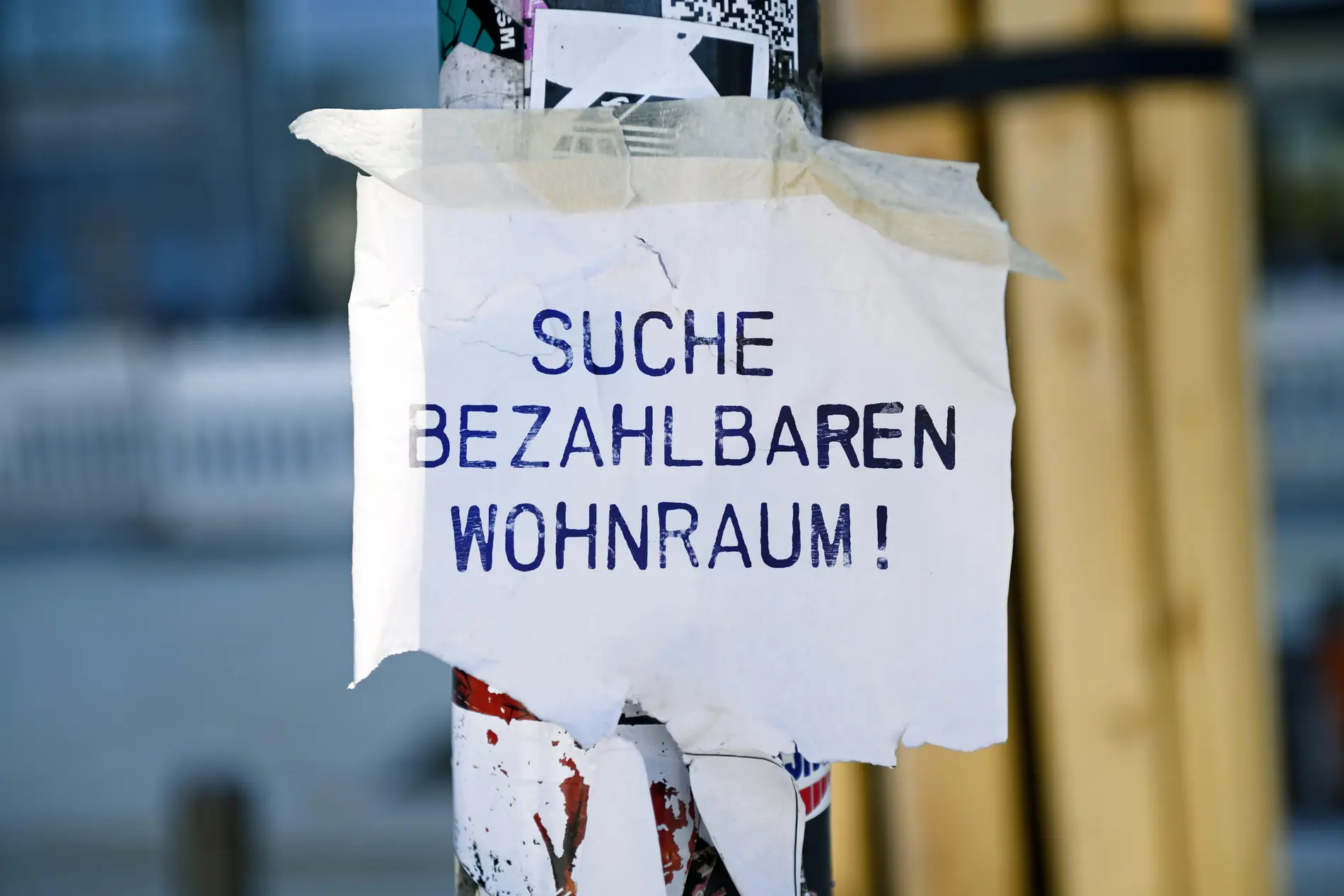 Suche nach bezahlbaren Wohnraum Flyer mit Aufschrift Suche bezahlbaren Wohnraum an einem Laternenmast.